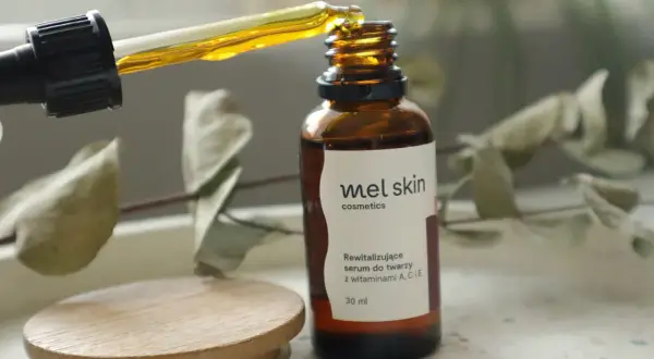 Kropla złotego serum z pipety wpada do brązowej buteleczki Mel Skin.