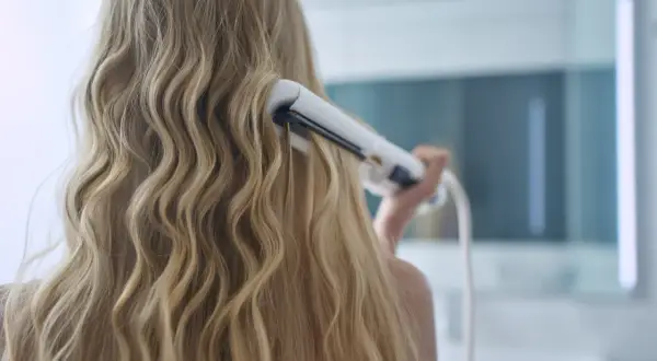 Kobieta kręci blond włosy lokówką z klipsem, tworząc fale.