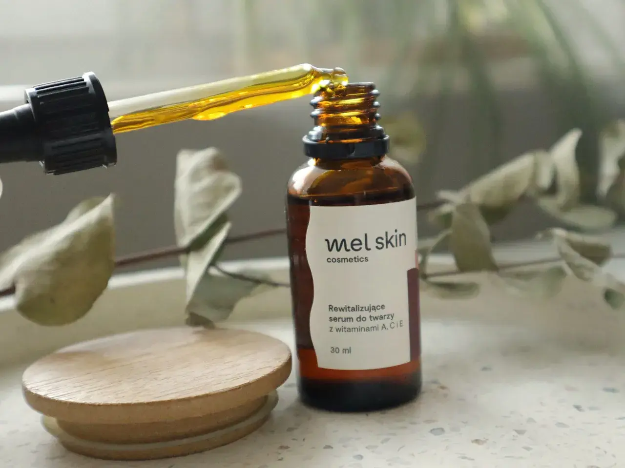 Kropla złotego serum z pipety wpada do brązowej buteleczki Mel Skin.
